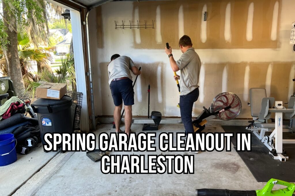 Two junk removal team members clearing out a cluttered garage in Charleston, SC during a spring cleanout, removing items like workout equipment, trash bins, and household debris.